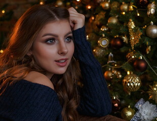Young beautiful girl with loose hair close up sitting at the Christmas tree with Christmas toys