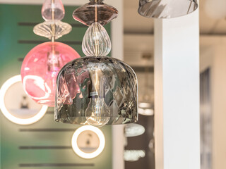 A group of switched-off multicolored lamps with a gray, pink glass ceiling is suspended in the interior. Concept of room decoration. Indooors. Close up.