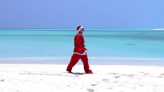 Santa Claus sitting on the beach with outstreched hands. Christmas holidays on islands