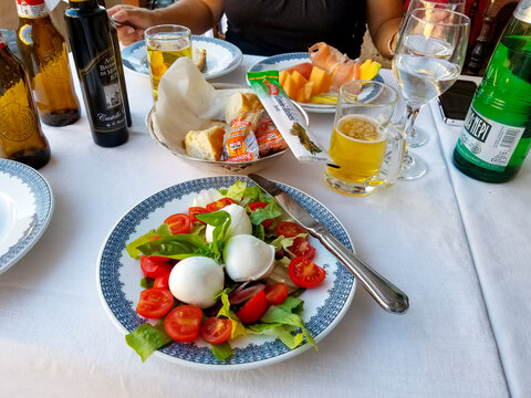 View of a full table of food and drinks including caprese salad, bread and melon on an outdoor cafe table in Rome Italy, on August 29 2019.