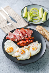Top angle view on sunny side up eggs prosciutto coppa Capocollo dry meat and homemade ajvar paprika salad on the table as dinner or breakfast meal