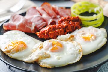 close up view on sunny side up eggs prosciutto coppa Capocollo dry meat and homemade ajvar paprika salad on the table as dinner or breakfast meal