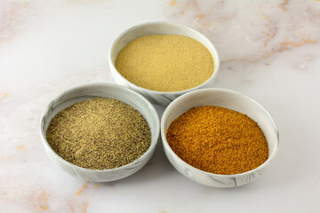 Ground white pepper, black peeper and red pepper spices in ingredient bowls on table