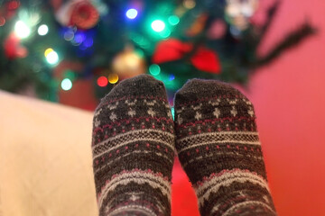 Feet in warm wool socks by the Christmas tree. Selective focus.