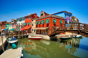 Fototapeta na wymiar Burano lagoon famous traditional vivid colorful houses vibrant colors island tourism landmark cityscape. Sea canal with boats and bright paint facade old historic scenic place. Venice Italy