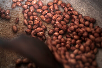 horizontal closeup photography of fresh soaked peanuts being roasted on a silver iron pot, with a wooden ladle, indoors in the Gambia, Africa