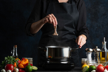 The chef in black uniform puts baby octopus into pan with boiling water. Backstage of preparing festive dinner with seafood at professional restaurant kitchen. Dark blue background. Frozen motion.