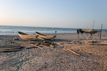 horizontal wide angle photography of a sea shore landscape, with wooden handmade boats and shade shelter made of palm trees, on an Atlantic beach, outdoors oj a sunny day in the Gambia, Africa