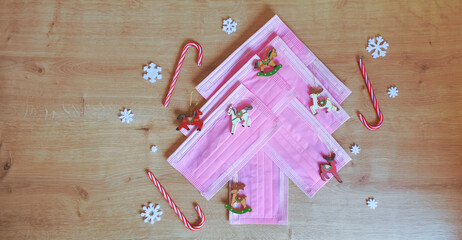 Christmas tree made of pink surgical masks with colorful vintage Christmas ornaments and decorations on a warm wooden background. Safe Christmas or medical background. 
