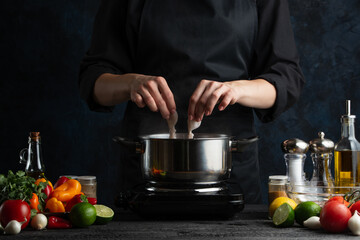 The chef in black uniform cooks octopuses in the saucepan. Backstage of preparing festive dinner with seafood at professional restaurant kitchen. Dark blue background. Frozen motion.