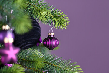 Close up of beautiful purple riffled glass tree bauble on decorated Christmas tree with other seasonal tree ornaments on violet background with empty copy space