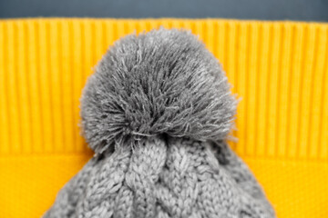 Close up of knitted gray hat with pompon on yellow sweater in trendy colors on grey background. Colors of the 2021 year. Cozy knitted clothes, warm concept.