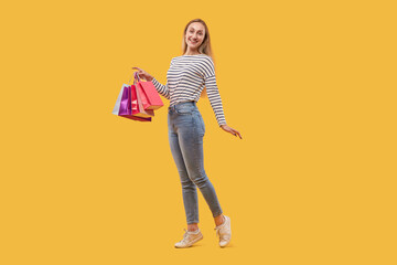 Happy beautiful young blonde woman with shopping bags in her hands. In full growth. Yellow isolated background.