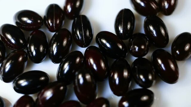 Black oval fusiform capsules in a gel shell close-up. Real time, natural light, white background, carotenoids, carotenoid pigments, Astaxanthin