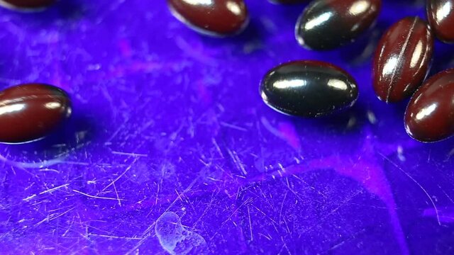 Maroon and black oval spindle-shaped capsules in a gel shiny shell extremely close-up. Real time, natural light, on a blue background, carotenoids, carotenoid pigments, Astaxanthin