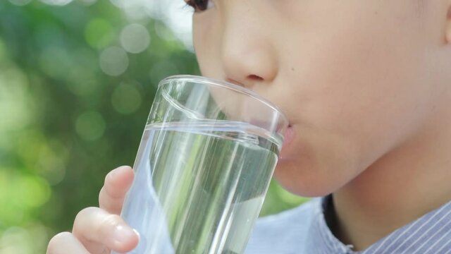 4k Selective focus, close up young Asian boy drink water from glass in the garden