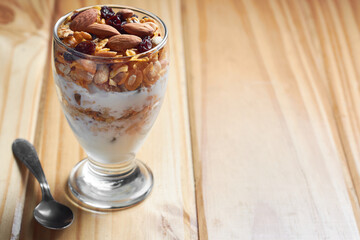Cup of granola and yogurt with raisins, almonds and peanuts on wooden table showing the concept of tasty, healthy food. Copy space.
