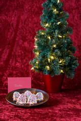 Tree shaped decorated sugar cookies left out for Santa, with a lighted tree, on a red background
