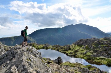 Young hiker at the top of mountain standing next to a little lake and admiring beautiful view. Lake...