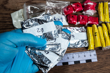 evidence of smuggling traffic: Packaging of a narcotic substance in the hand of a forensic expert against the background of other arrested materials, cocaine, heroin, spice