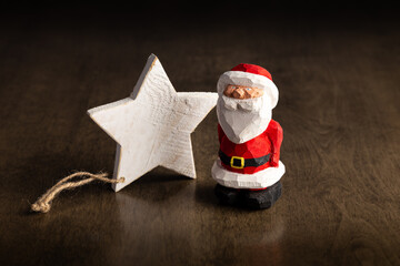 Carved wooden Santa Claus standing to the right of a white painted star.