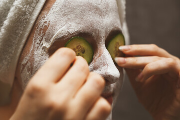 A woman applies a face mask and uses cucumber slices to solve skin problems around the eyes. An ecological, vegan, vegetarian way of life. Self-care and lifestyle, solving skin issues.