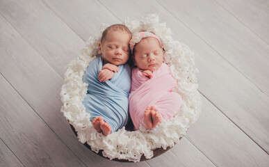 Twins are newborn brother and sister. Newborn girl and boy. Sleeping sweetly in a basket.