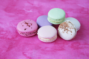 multicolored macaroons or macarons on a pink background with copy space for text. delicious french dessert. close-up.