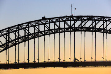 Closeup of the Sydney Harbour Bridge, silhouetted against a sunset sky. A party of bridge climbers can just be seen near the flagpoles