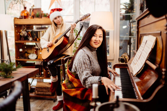 two young women play the piano and guitar in a country house.