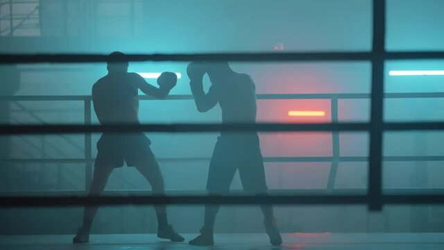 Boxer in the boxing gym. Bandages his hands. Sparring in the ring. Boxer jumping rope. Exercise with ropes. Round one. Fog in the ring. Zetsky sport. Beautiful backlight. World boxing champion.

