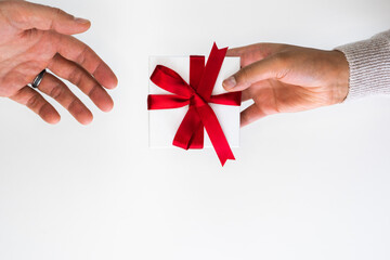 Beautiful holiday or Christmas background image of a mixed race African American woman handing a small red ribbon wrapped gift box to a Caucasian male's open hand on a white backdrop with copy space.