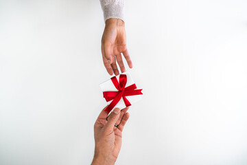 Beautiful holiday or Christmas background image close up of hands from a mixed race African American woman tying a bow with red ribbon onto a small white gift box with white backdrop and copy space.