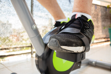 Adult man practicing stationary bike at home in times of pandemic and Covid. Side view of feet exercising.