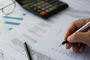 Financial accounting, Closeup, A man holding a pen and checking the list financial transaction, A calculator, pencil, glasses on paper, Graphs showing statistics of financial, Blurred background