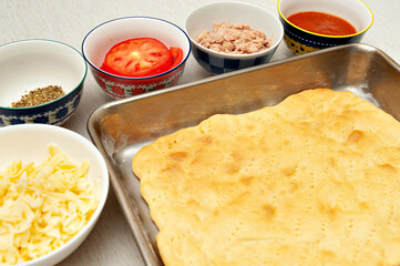 Homemade rectangular pizza - Pizza dough and ingredients: cheese, oregano, sliced tomatoes, tuna fish and tomato sauce