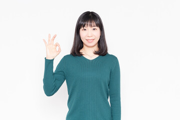 白背景の前に立ってOKのジェスチャーをする女性