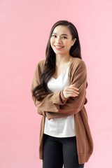 Fototapeta premium Portrait of a smiling asian businesswoman standing with arms folded and looking at camera isolated over pink background