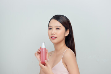 Young pretty stylish woman  over white wall background holding bottle with cosmetics water.