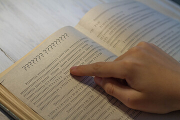 An open book with an incomprehensible text of question marks, a person tries to read the book.