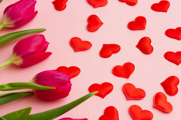 Fototapeta na wymiar a group of red fresh tender tulips with green leaves lie on a pastel pink background with small hearts. Valentine's day concept. View from above