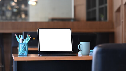 Stylish workspace with computer tablet, stationery and coffee cup on wooden table. Blank screen for graphics display montage.
