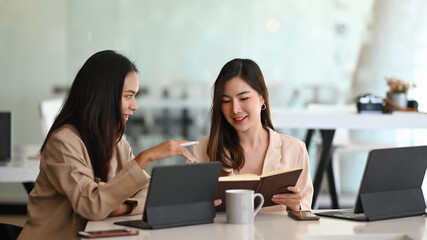 Two businesswomen employees colleagues using computer tablet and discussing working together on business project.