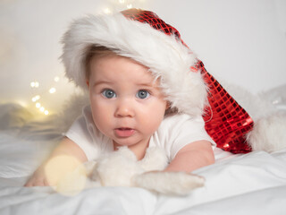 Adorable baby girl in Santa hat lying on the bed