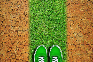 Green sneakers on way from grass in dry cracked earth. Global warming or change climate concept.