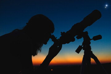 Woman looking at night sky with amateur astronomical telescope.
