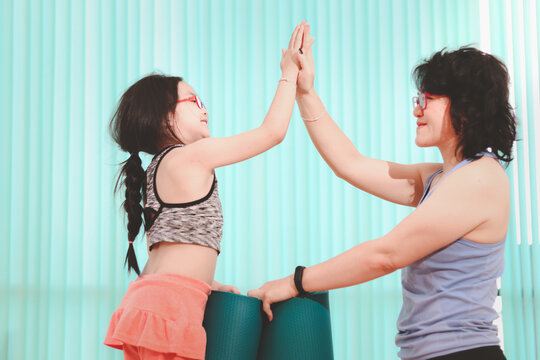 Mother and daughter giving high five after rolling yoga mat, exercise at indoor studio, happy spending time together, sporty family practicing yoga, working out and exercising for taking care of their