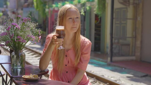 Young woman traveler drinks coffee sitting by the railway paths which go through residential area in Hanoi city. Hanoi Train Street is a famous tourist destination