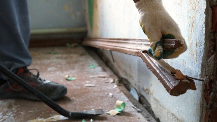 manual scraping of the skirting board in the old room with a scrap in the hands of a worker,...