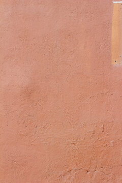 Full frame texture background of an eroding exterior concrete wall with cracked and peeling red painted adobe plaster surface, in natural sunlight